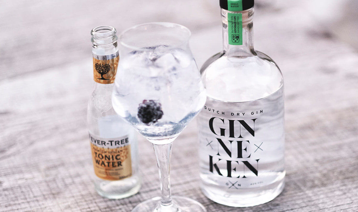 Een chique G&T met ijs en bramen staat naast flessen; ontdek meer op GinnekenGin.com.