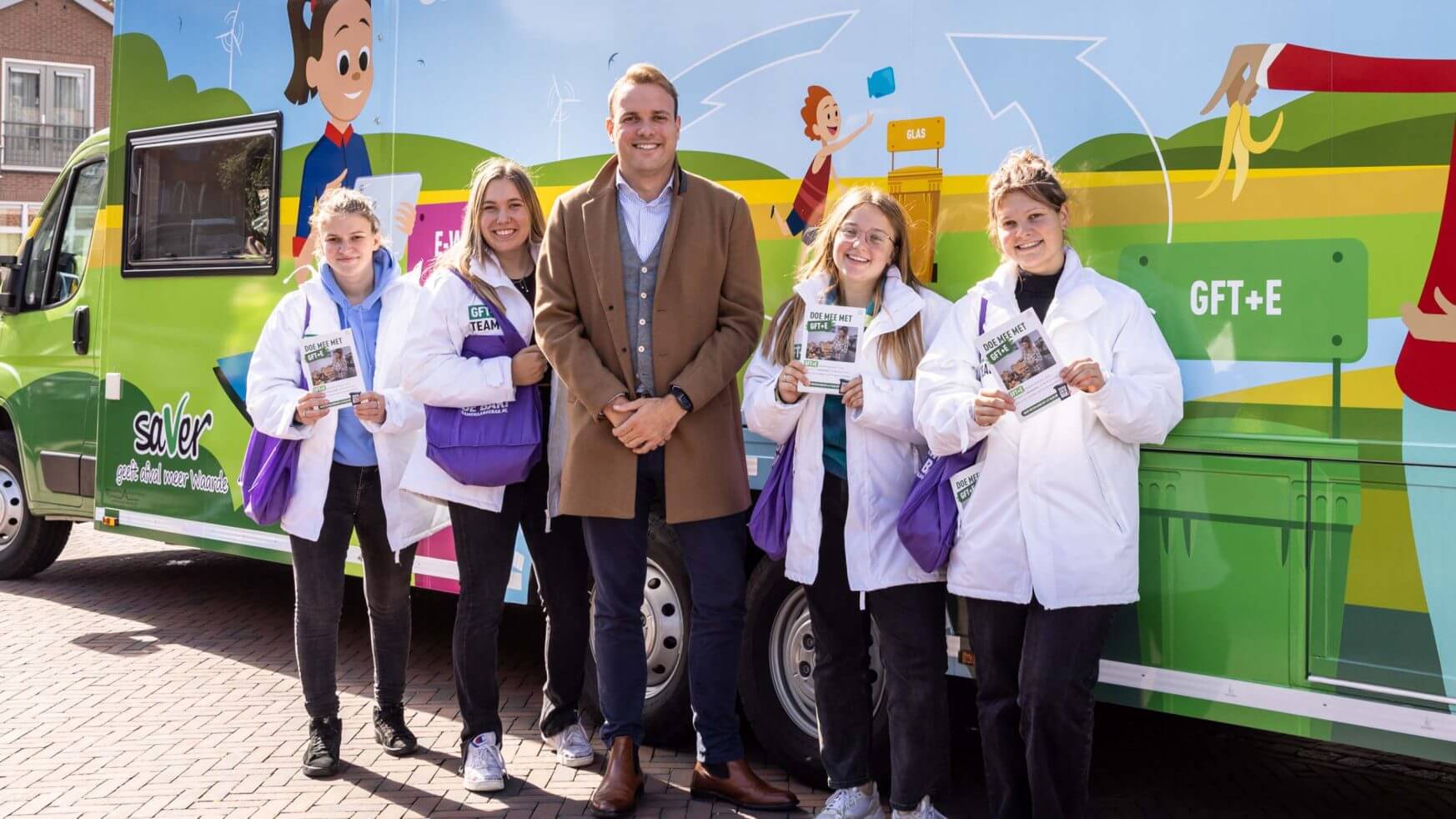 Vijf lachende mensen poseren bij een kleurrijk busje, met pamfletten in de hand en in "RSD aan de bak!"-kleding.