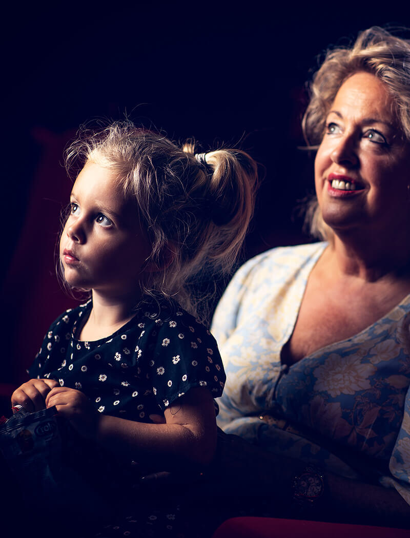 In een donkere ruimte zitten een vrouw en een meisje dicht bij elkaar, hun ogen gericht op elkaar, en ze delen een moment van diepe concentratie.