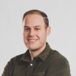 Persoon in een groen shirt die lacht tegen een eenvoudige achtergrond.