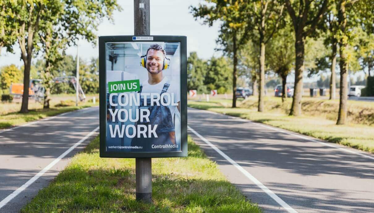 Reclamebord: Werknemer in overall, "Kom bij ons. Bepaal uw eigen werk.