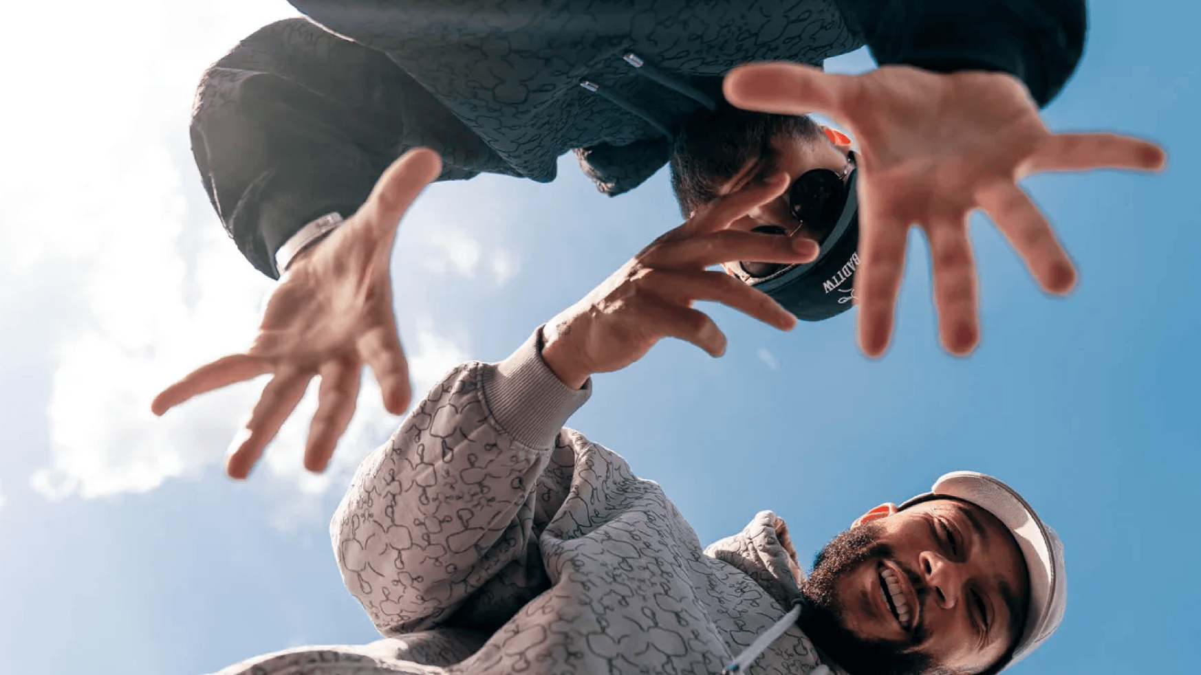 Twee mannen in Memphis Depay-shirts glimlachen en reiken naar de camera onder een strakblauwe hemel.