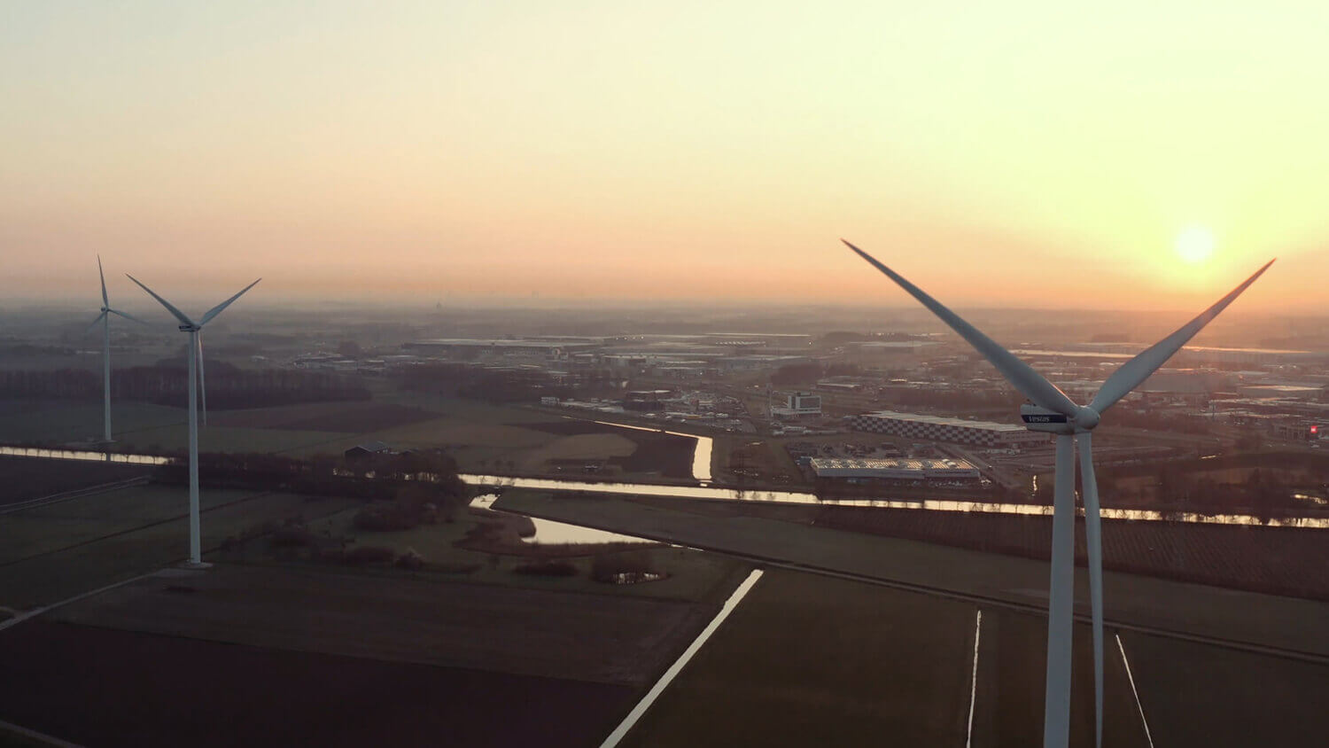 Een serene zonsondergang werpt een warme gloed over de velden en windturbines en symboliseert de rust van het platteland.