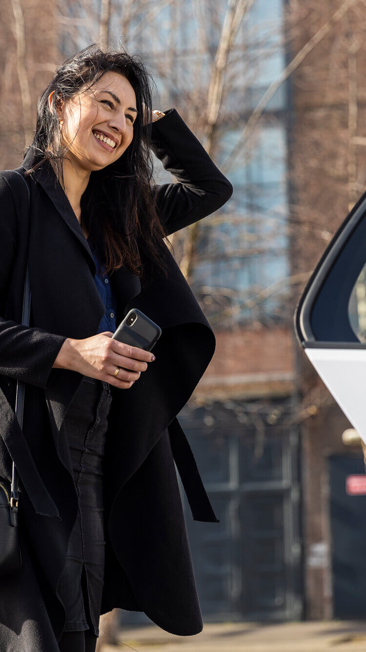 Een vrouw straalt naast een taxistandplaats, terwijl ze haar telefoon in de warme zon vasthoudt.
