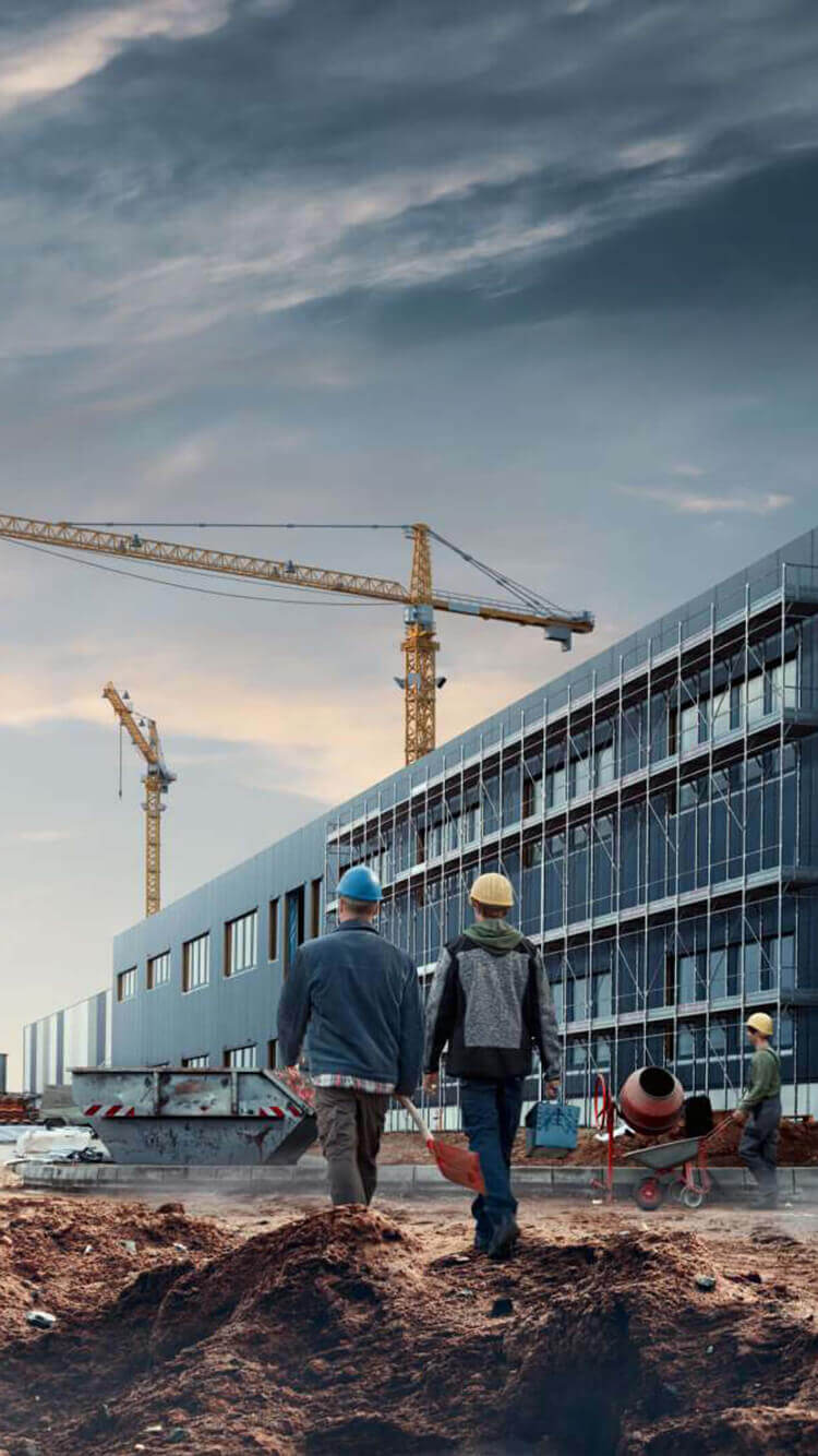 Werknemers van de Elkor Groep, gehuld in helmen, zijn onderweg naar een bouwplaats die omringd is door kranen en onder een gedeeltelijk bewolkte hemel.