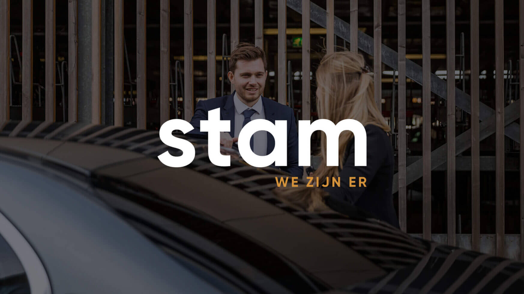 Twee mensen praten bij een poortje met de tekst "Stam We Zijn Er", waarschijnlijk wachtend op hun Taxi Stam-rit.