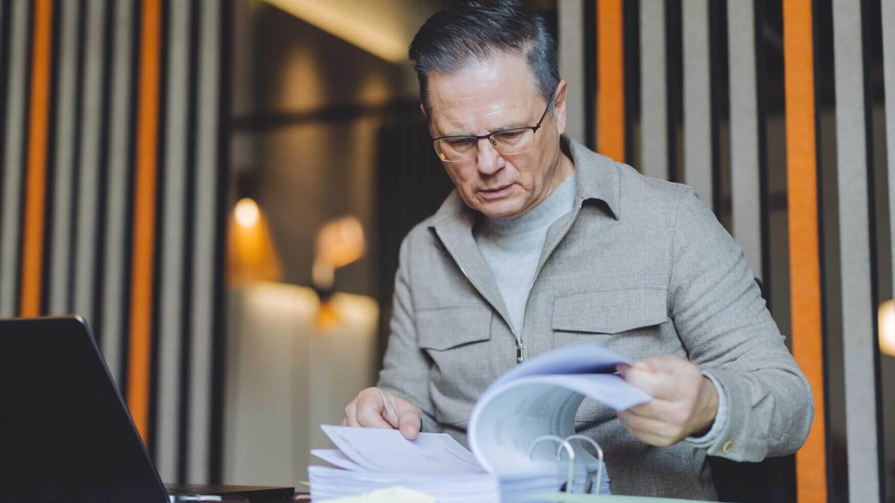 In een strak kantoor van TunnelmaDesign bekijkt een man met een bril documenten, met zijn laptop naast zich.
