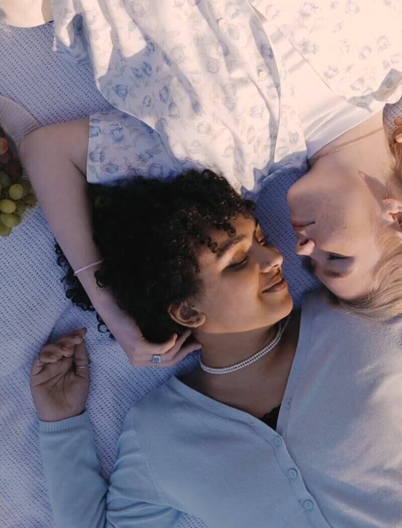 Twee mensen liggen lachend tegenover elkaar op een deken, met druiven in de buurt.