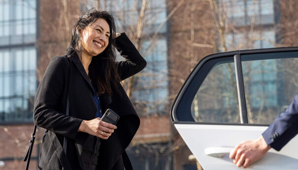 Een lachende vrouw, met haar telefoon in haar hand bij een open autodeur, geniet van de zon. Ze is klaar voor een nieuw avontuur.