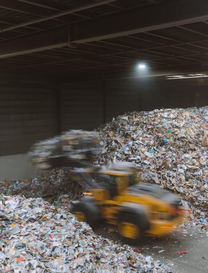 Een voorlader verplaatst gemengd papierafval in een slecht verlichte recyclingfaciliteit.