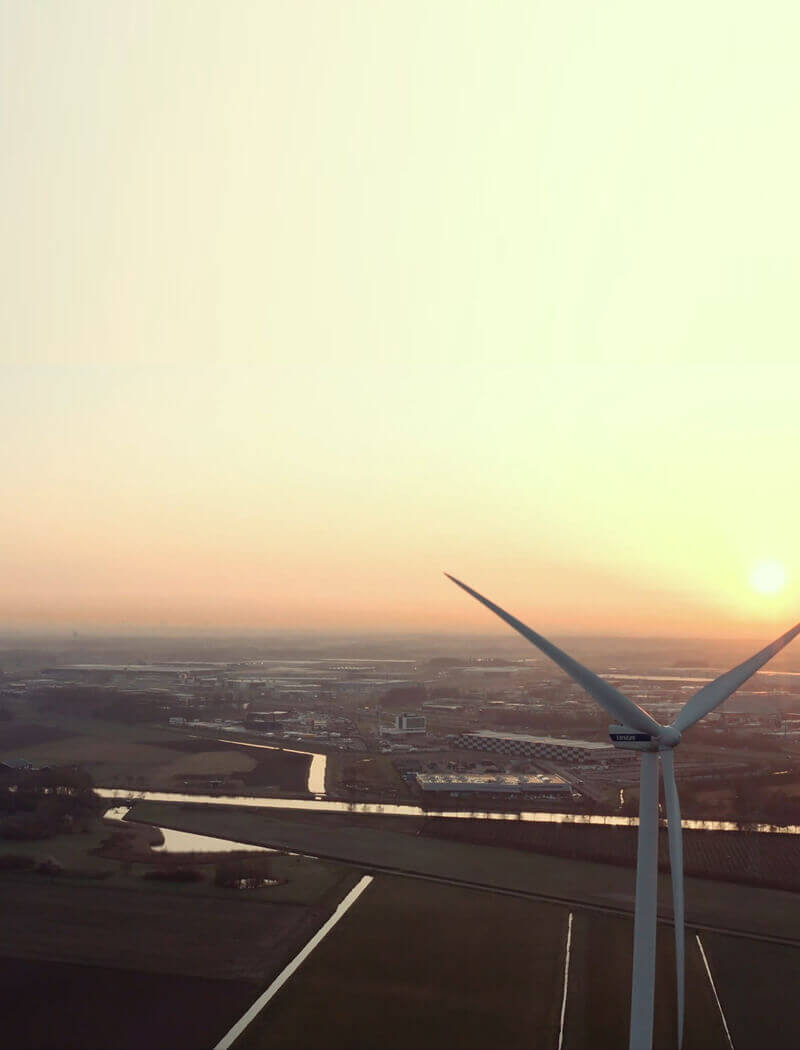 De windturbine staat hoog in een uitgestrekte, landelijke dageraad, omringd door velden en waterkanalen.