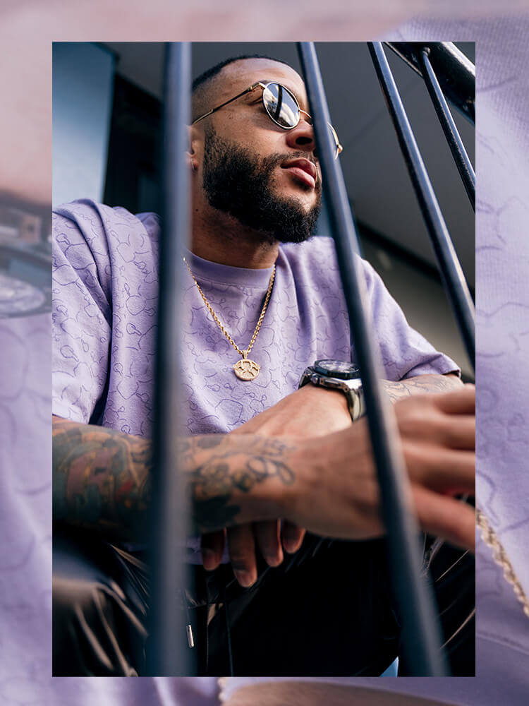 Getatoeëerde man met zonnebril en lila shirt zit achter de tralies en kijkt omhoog.