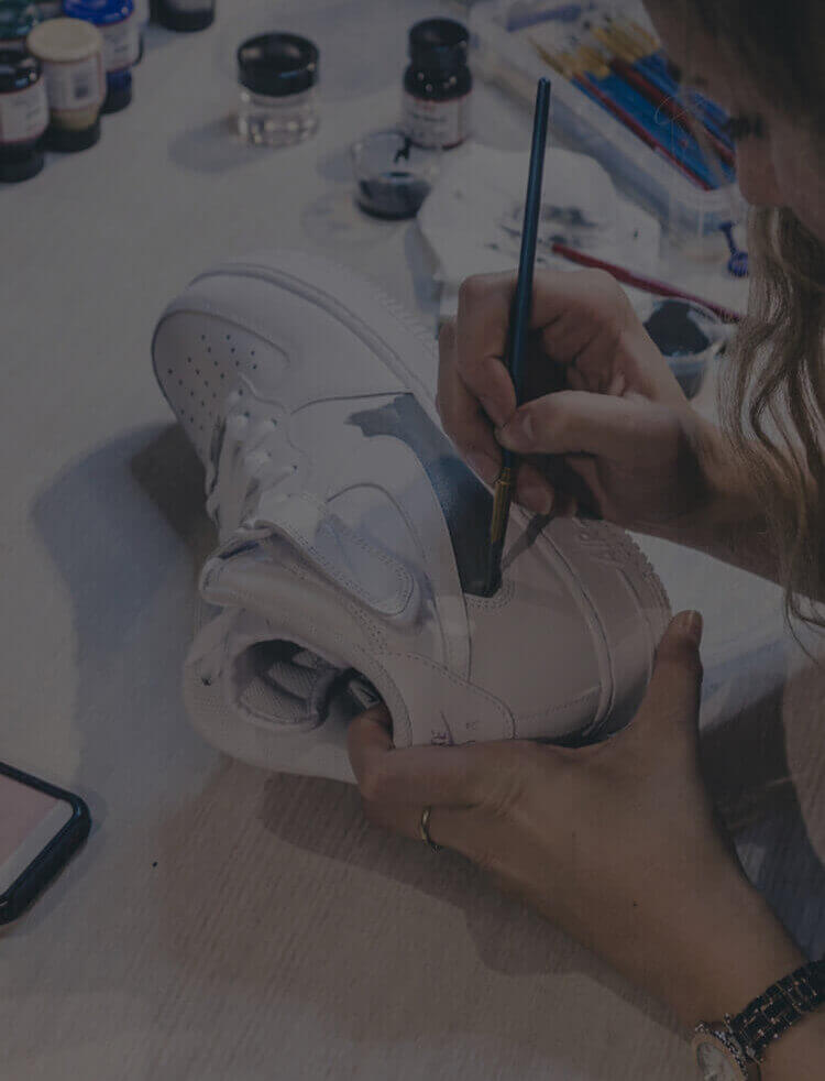 Iemand knapt een witte sneaker op met een kwast en creëert zo een uniek exemplaar voor de exclusieve Customs by BB-lijn.