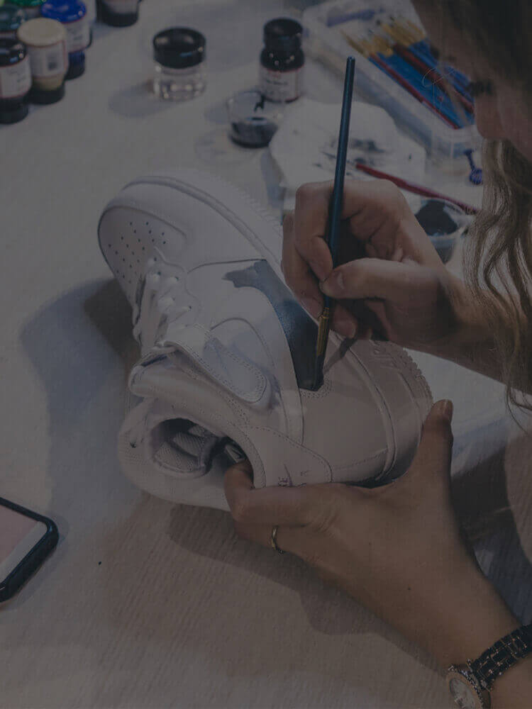 Iemand knapt een witte sneaker op met een kwast en creëert zo een uniek exemplaar voor de exclusieve Customs by BB-lijn.