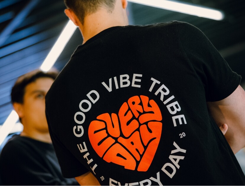 Ik draag een zwart T-shirt met de tekst "THE GOOD VIBE TRIBE EVERY DAY" en een rode graphic op de achterkant.