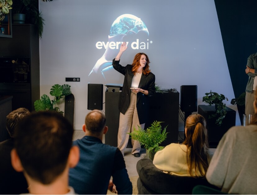 Een vrouw presenteert aan een zittend publiek. Achter haar staat een scherm waarop 'elke dag' wordt getoond.