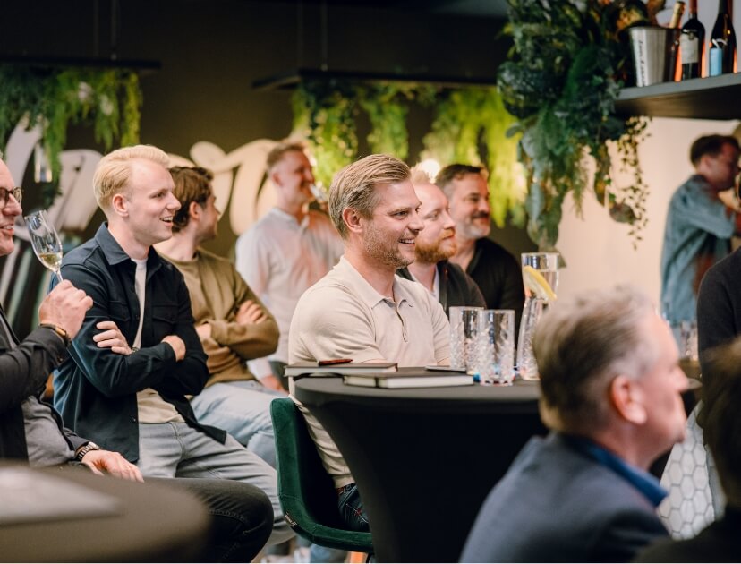 Een groep vrienden ontspant en lacht samen op een stijlvolle, met planten gevulde locatie.