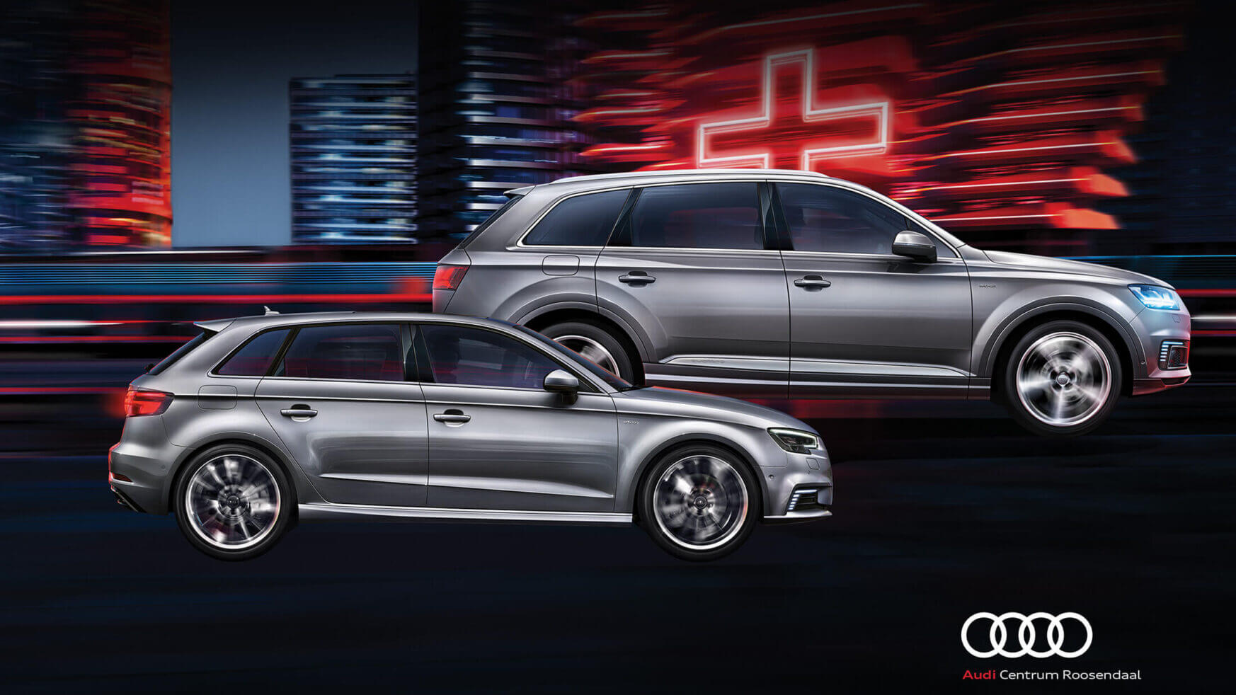Twee zilveren Audi's glijden door neonverlichte stadsstraten en stralen elegantie uit. Ontdek premium stijl bij Audi Roosendaal.