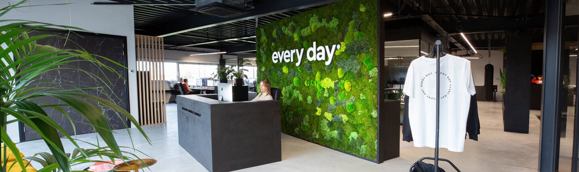 Moderne kantoorlobby: moswand met dagelijkse tekst, strakke receptiebalie versierd met planten.