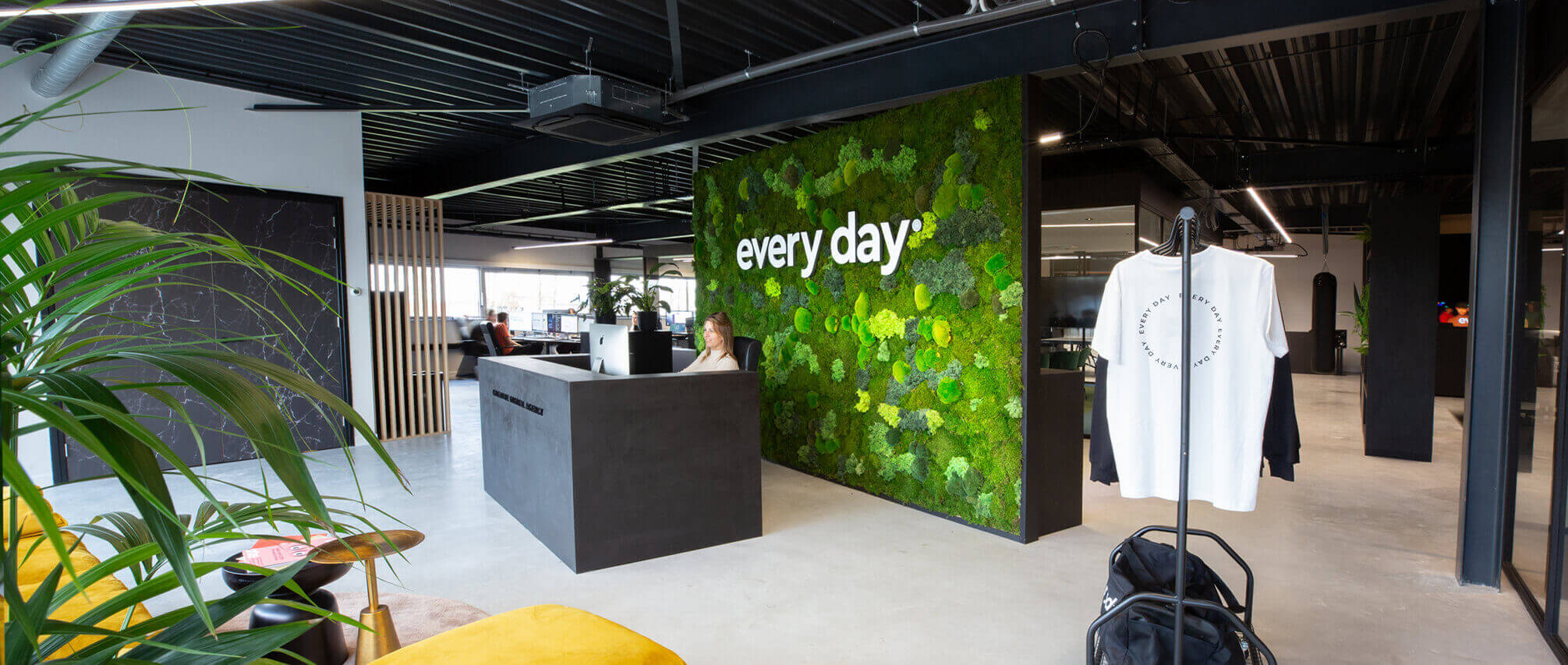 Moderne kantoorlobby: moswand met dagelijkse tekst, strakke receptiebalie versierd met planten.