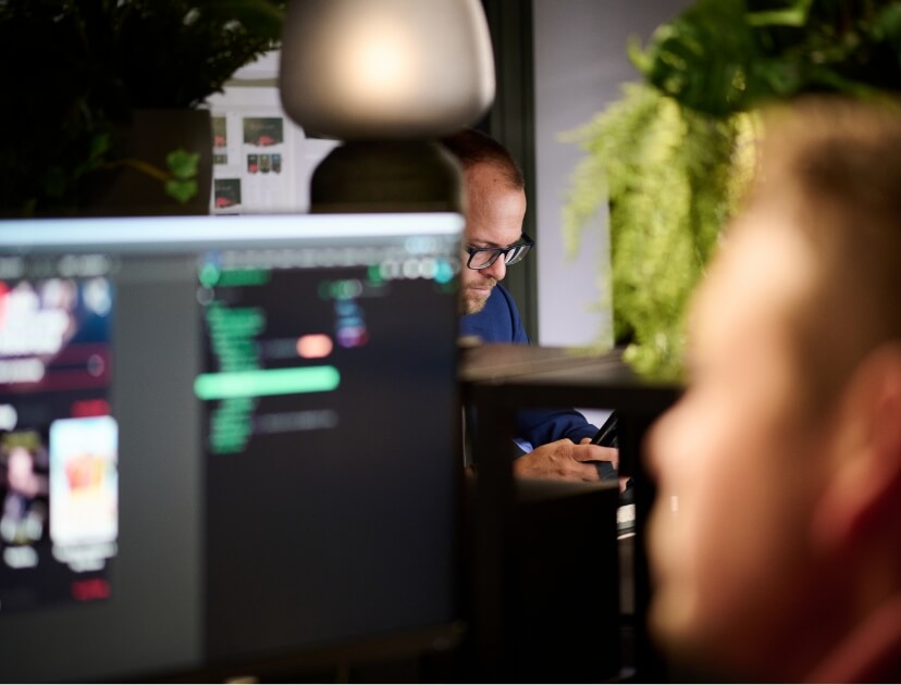 Een man met een bril werkt aan een bureau en programmeert op een wazig computerscherm.