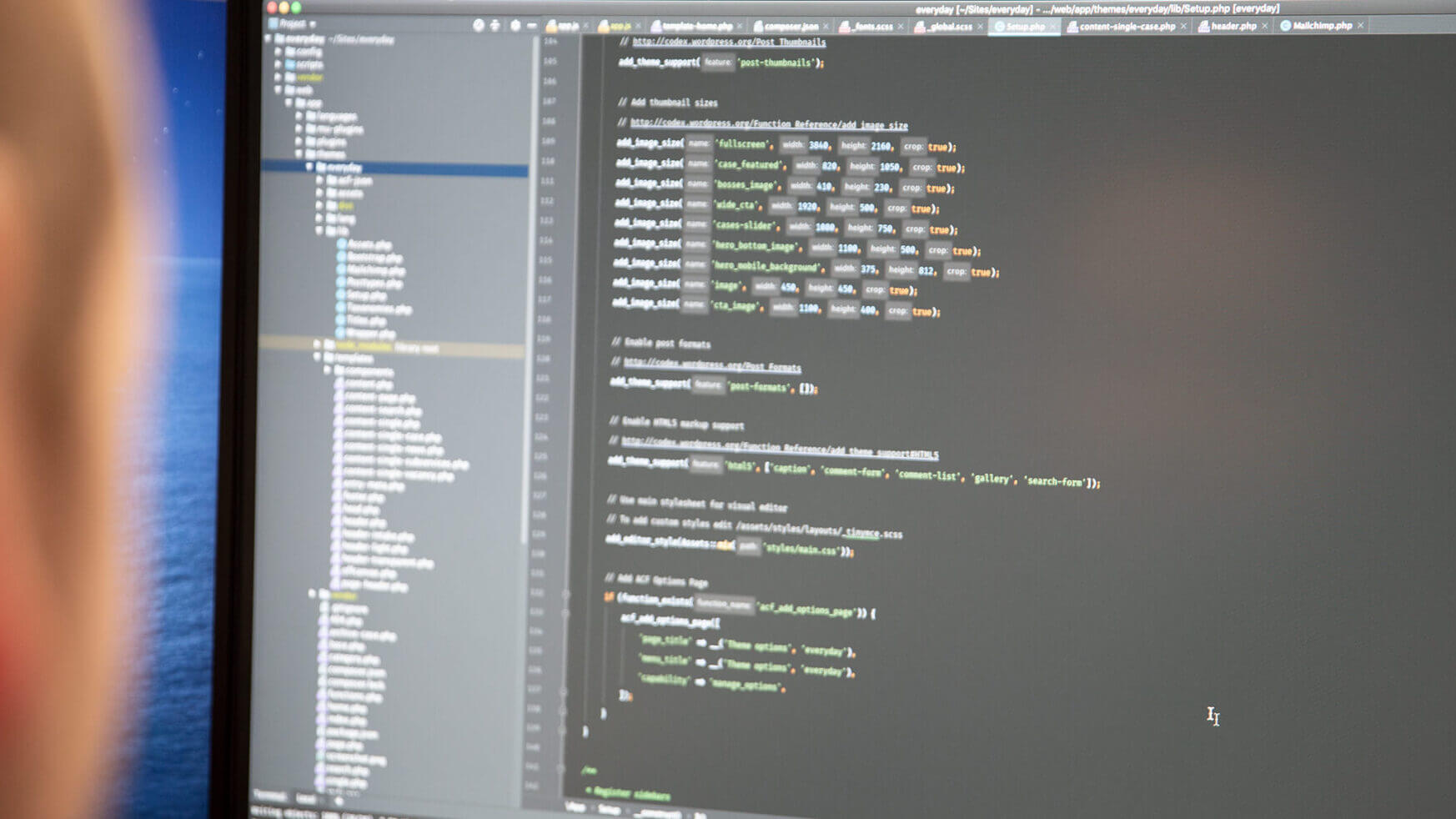 Een webdesigner programmeert aandachtig, met zijn ogen gericht op het scherm en een directory-boom ernaast.