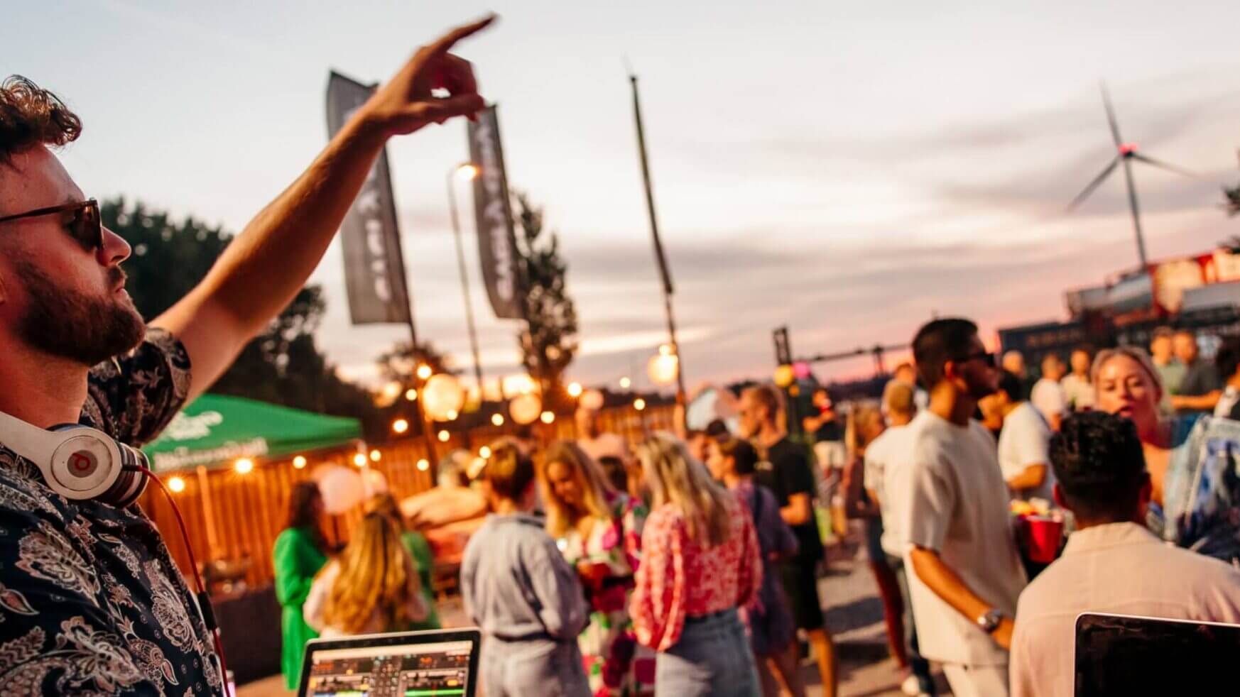 DJ draait op een bruisend buitenfeest, met een energiek publiek en warme avondverlichting.