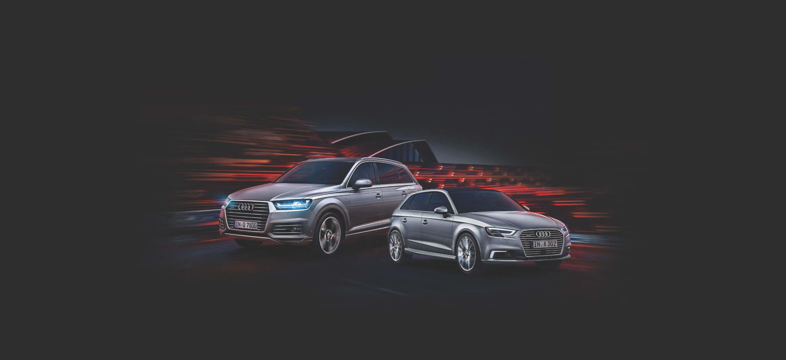 Twee zilveren Audi's racen over een donkere achtergrond, waarbij het strakke design en de dynamische prestaties centraal staan.