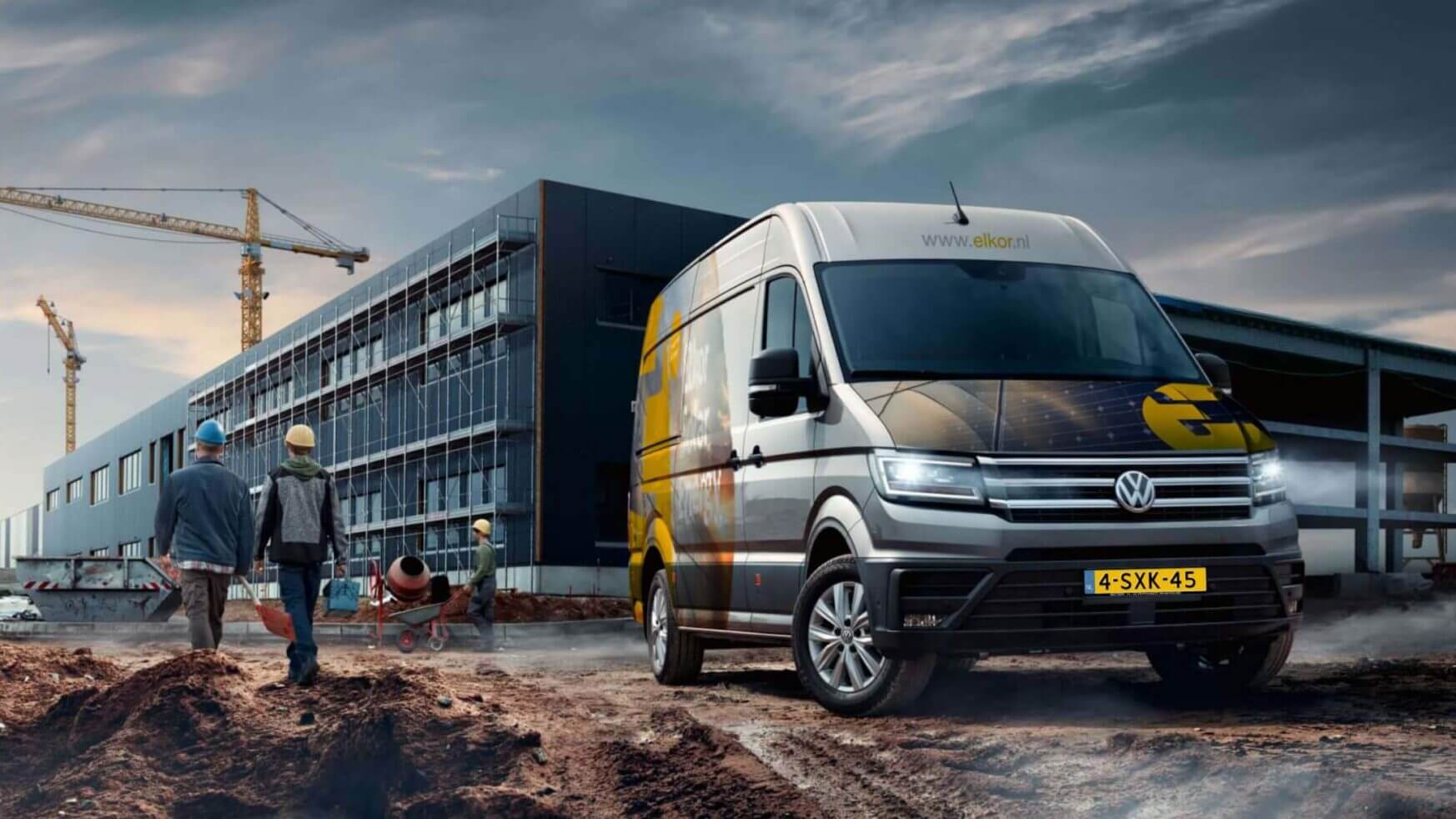 Een Volkswagenbusje met het logo van Elkor Groep staat geparkeerd op een bouwterrein met arbeiders, kranen en een gebouw.