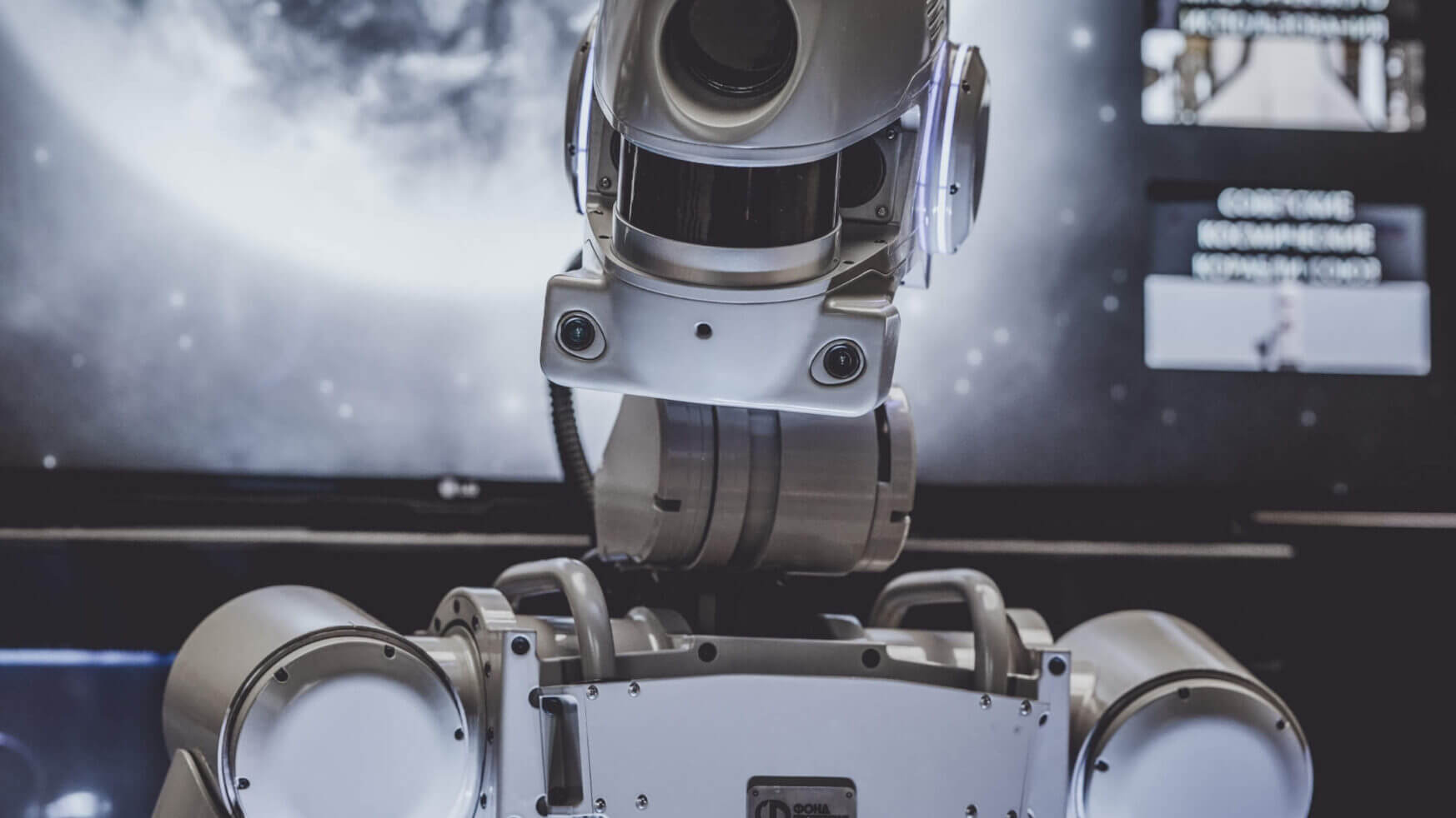 Een humanoïde robot staat voor een scherm waarop een grote afbeelding van de maan te zien is.