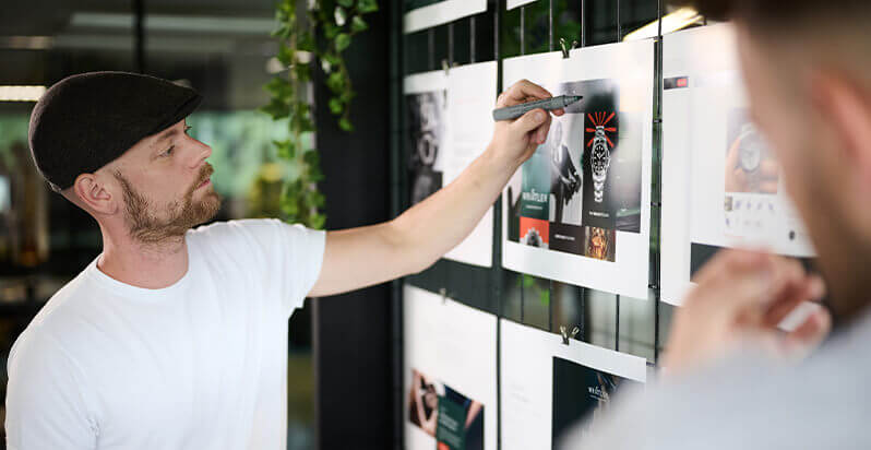 Man met platte pet schetst met pen ontwerpen op de muur.