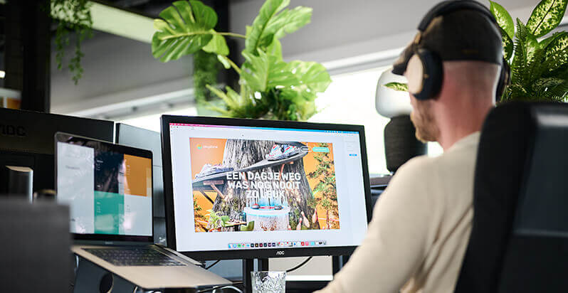 Koptelefoon op, werkend op een computer met een levendig webdesign, omringd door weelderige planten.