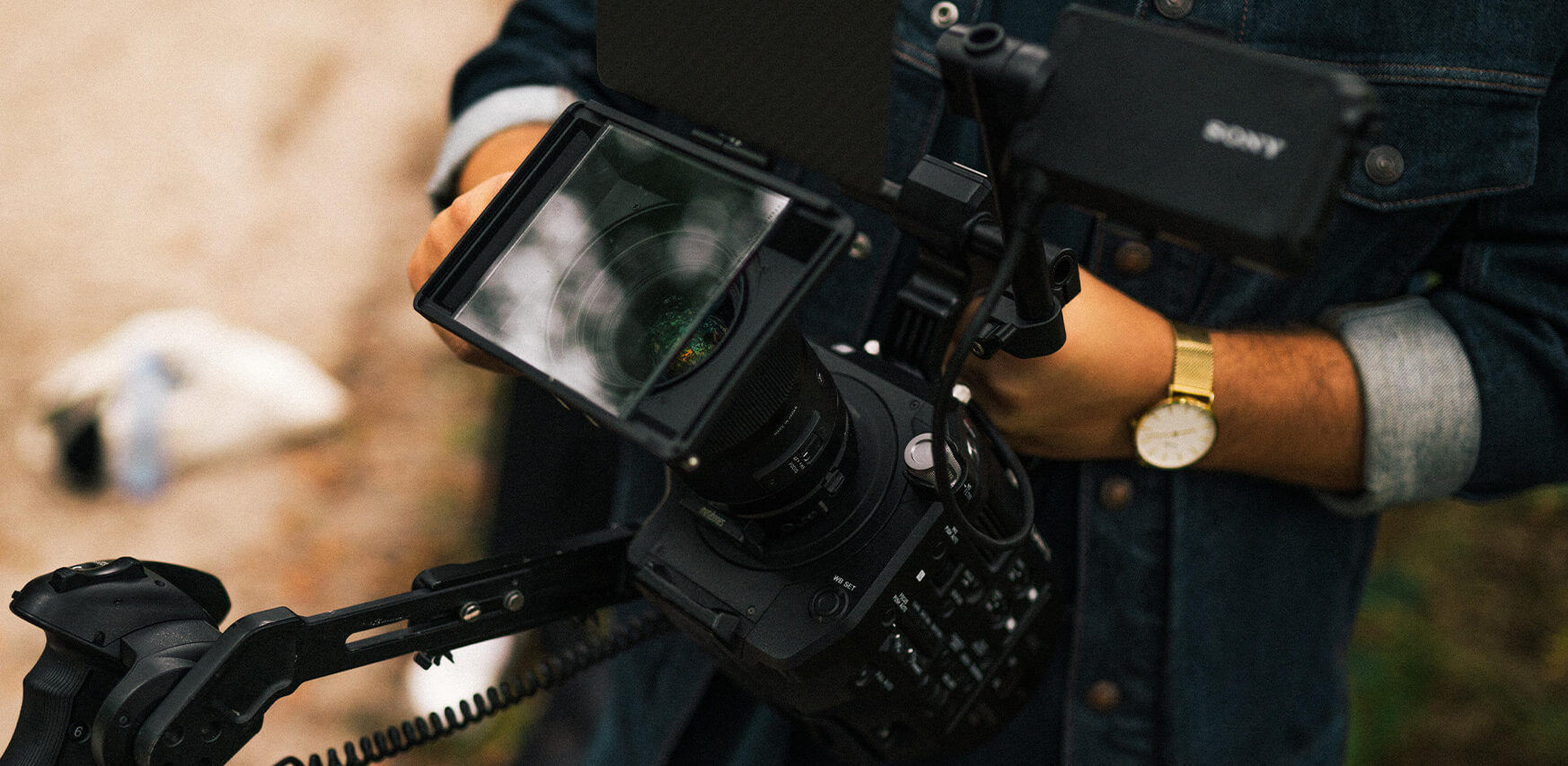 Een professional, gekleed in spijkerbroek, filmt outdoor-ontwerpen met grote scherpte, waarbij het camerascherm de reflectie van de lens laat zien.