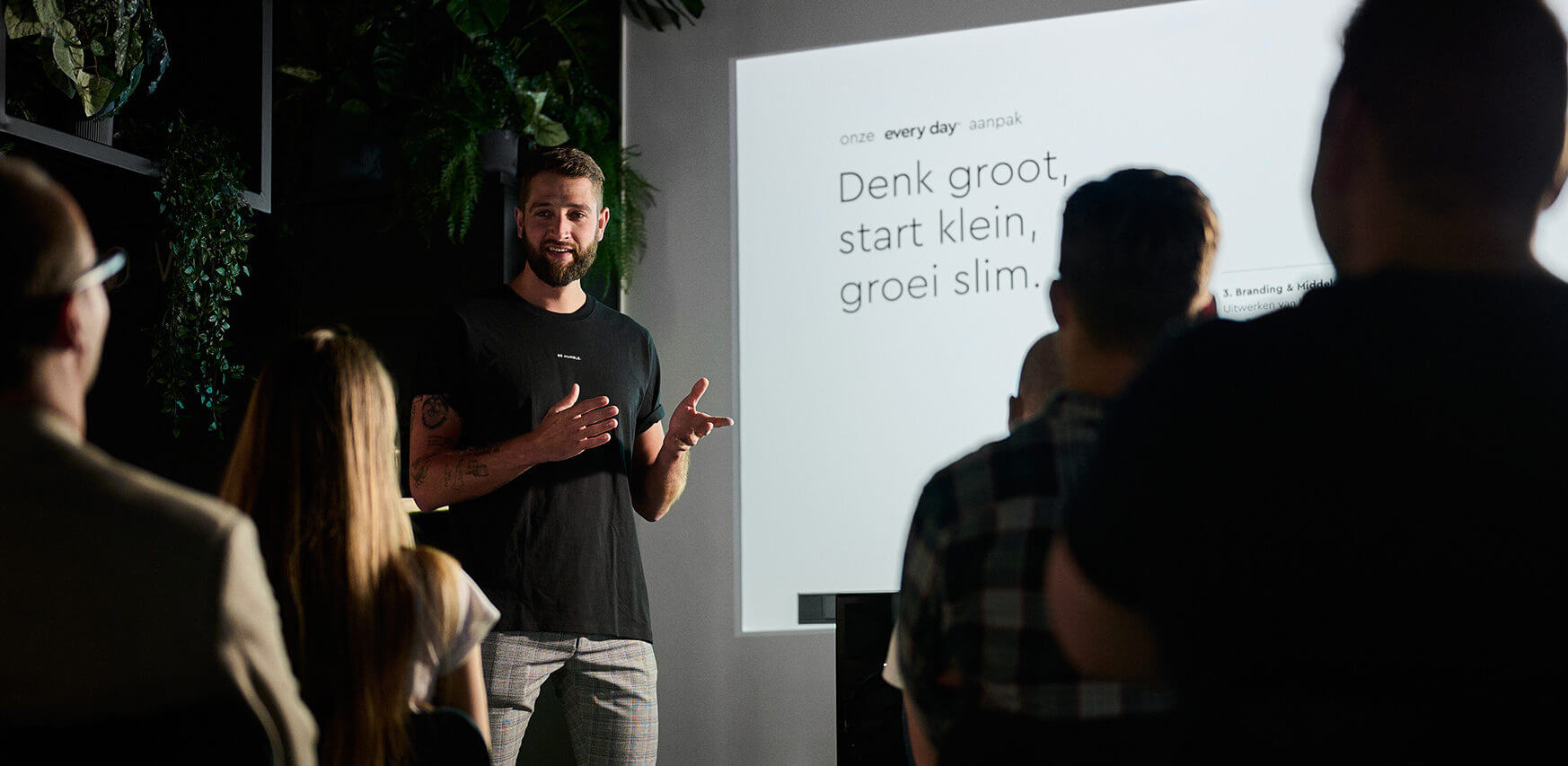 Een man geeft een presentatie aan een publiek en projecteert tekst op een scherm.