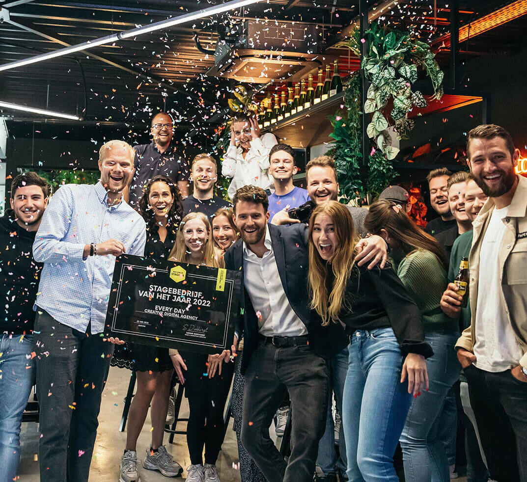 Een vrolijke groep poseert met een plaquette erin, omringd door confetti en brede glimlachen.