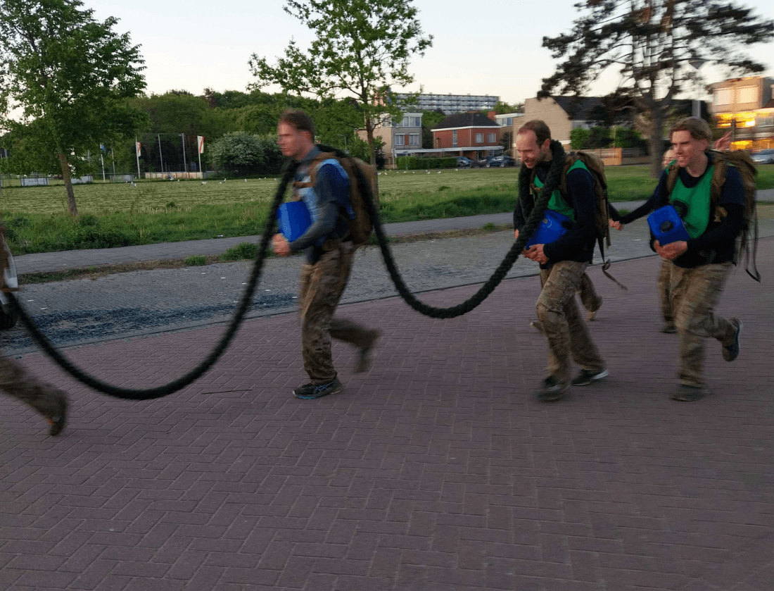 Drie mensen in camouflagebroeken lopen in een rij naar buiten, elk met een dik touw in de hand.