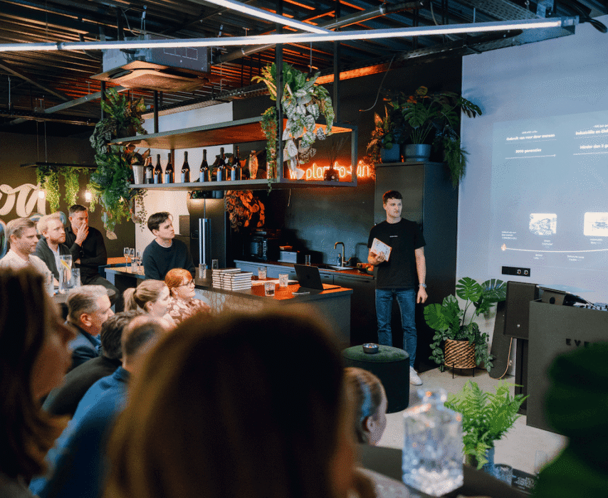 Man presenteert aan groep in een trendy, met planten gevulde kamer met een groot scherm.