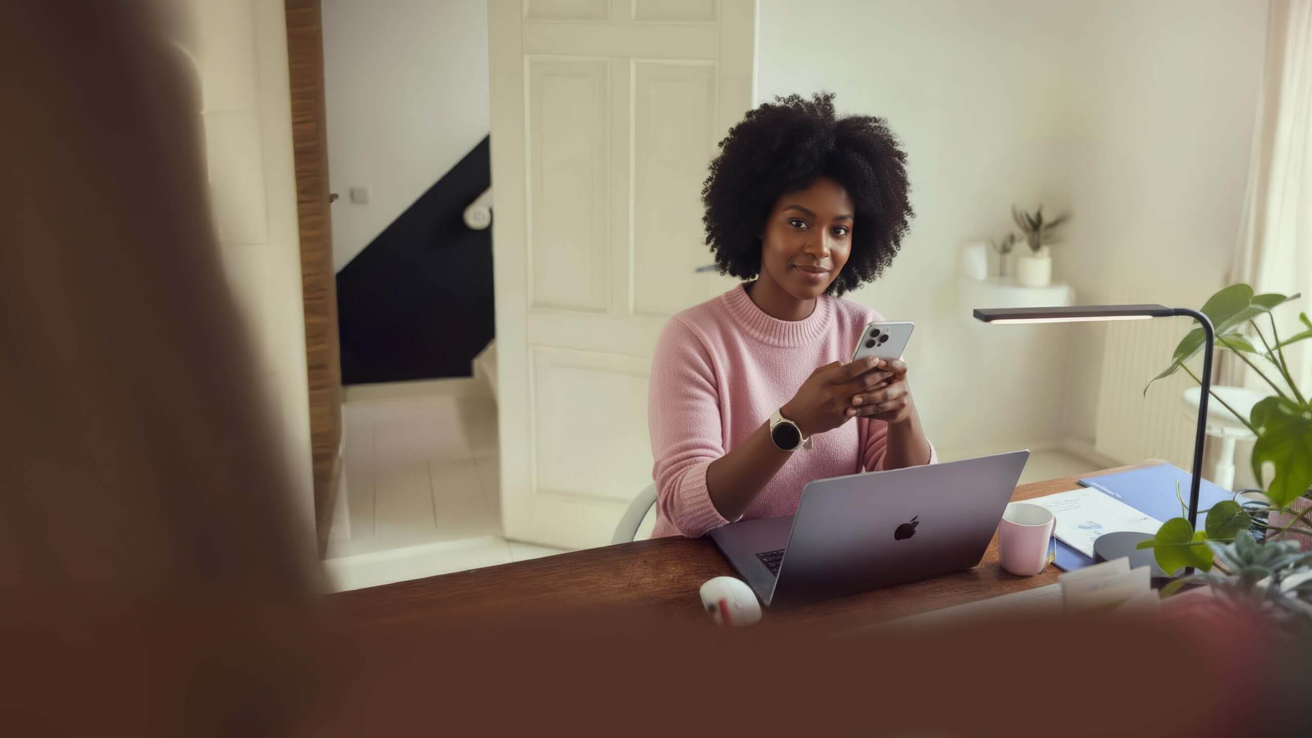 Glimlachende vrouw aan bureau met laptop en smartphone.