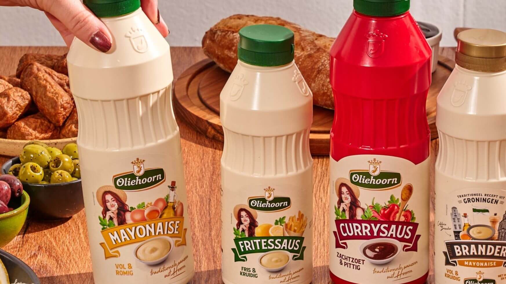 Oliehoorn mayonaise, fritessaus en curryflessen op een houten tafel met voedsel onscherp op de achtergrond.