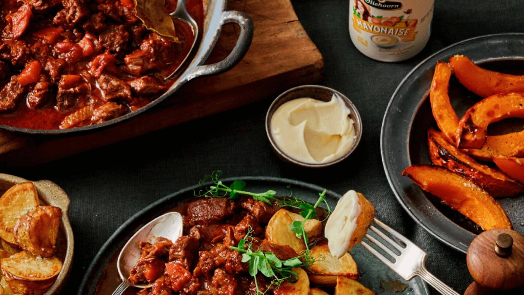 Runderstoofpot, geroosterde aardappelen en pompoenschijfjes op een bord; mayo en stoofpot in pannetjes ernaast.