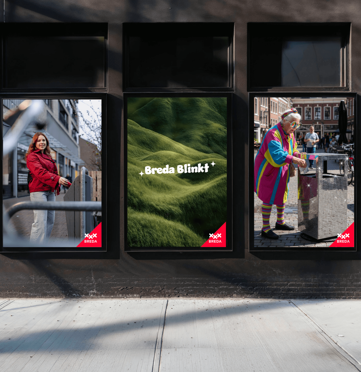 Drie ingelijste posters op een donkere muur: vrouw in rood, groene heuvels met tekst Breda Blinkt, persoon in kleurrijke outfit.
