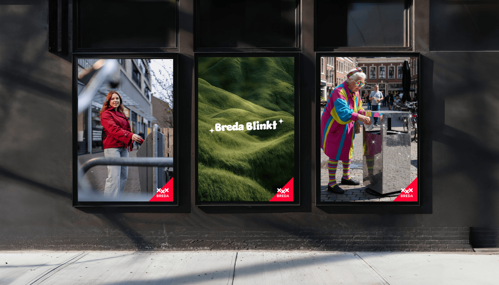 Drie ingelijste posters op een donkere muur: vrouw in rood, groene heuvels met tekst Breda Blinkt, persoon in kleurrijke outfit.
