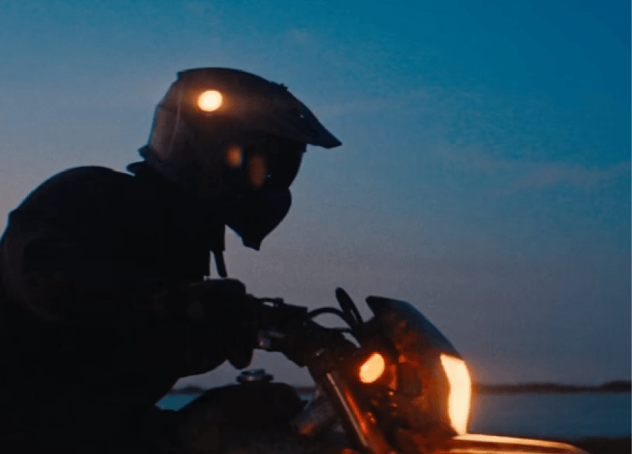 Silhouet van gehelmde motorrijder in de schemering met schijnende koplampen.