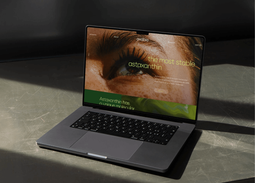 Laptop op grijs oppervlak toont een website met een close-up van een oog en tekst: "de meest stabiele astaxanthine.