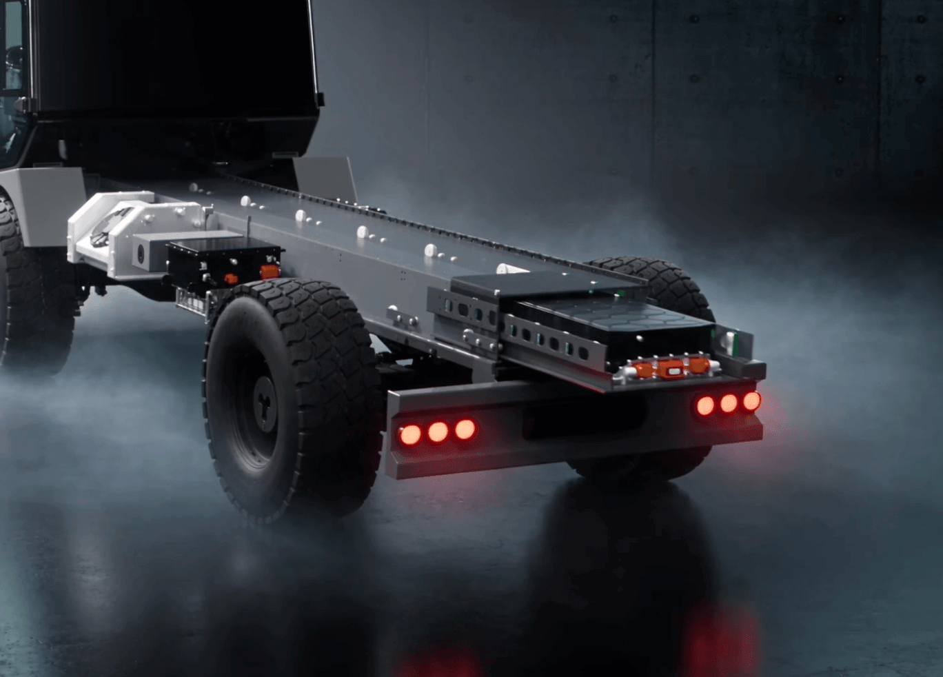 Een vrachtwagenchassis met achterwielen en rode lichten in een mistige, donkere omgeving, waaruit de intense energie van XNRGY Padel straalt.
