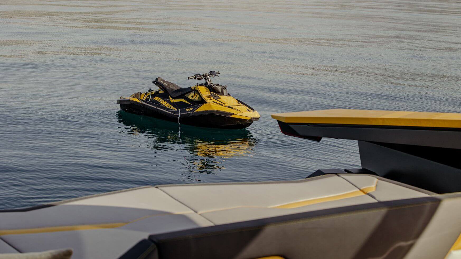 Een geel-zwarte Sea-Doo-jetski op rustig water naast het dek van een boot.