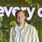 Een glimlachende man die poseert voor een groene mosmuur waarop het woord every in grote witte letters staat.