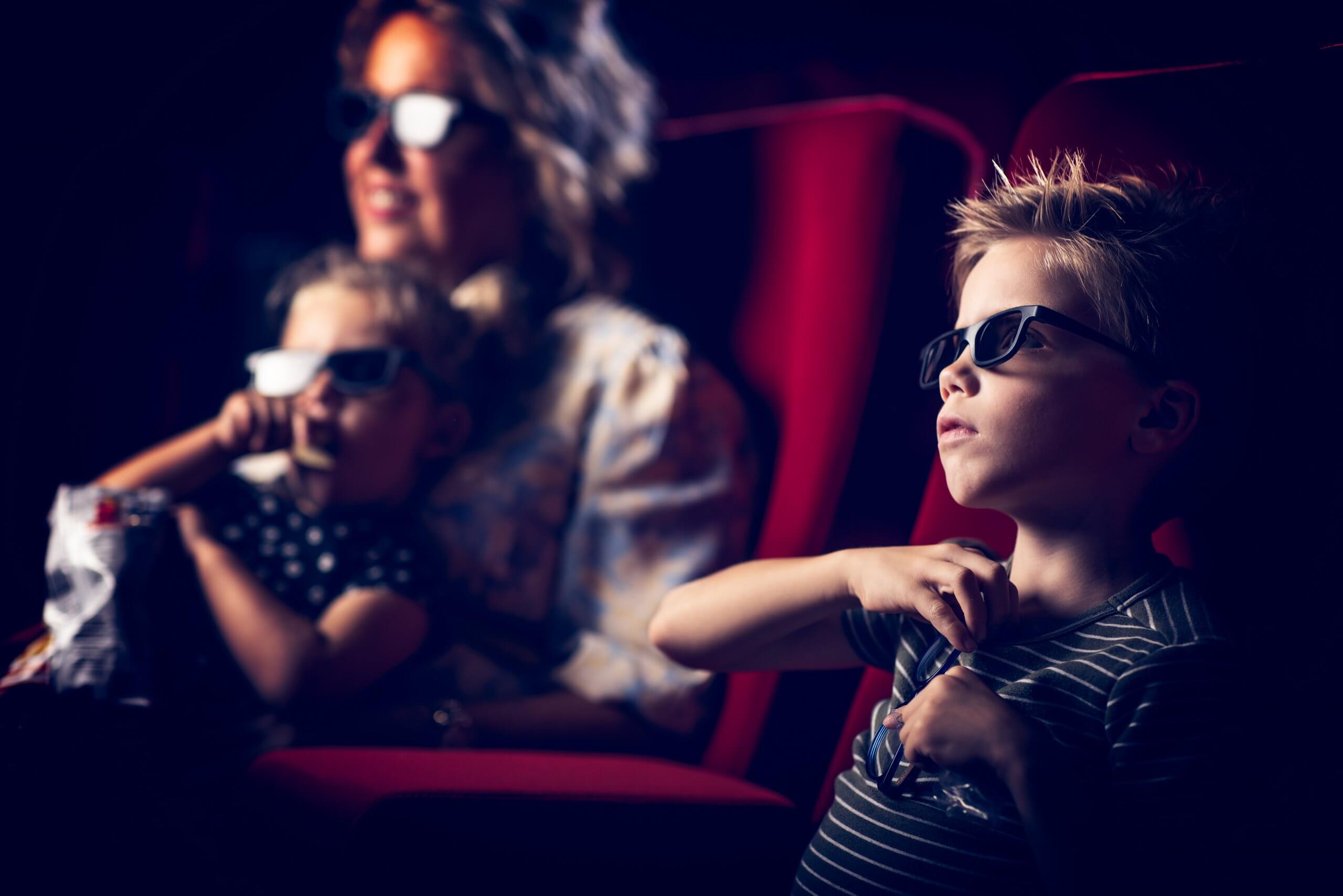 Een gezin met een 3D-bril kijkt aandachtig in een donkere bioscoopzaal. Een kind houdt popcorn vast.