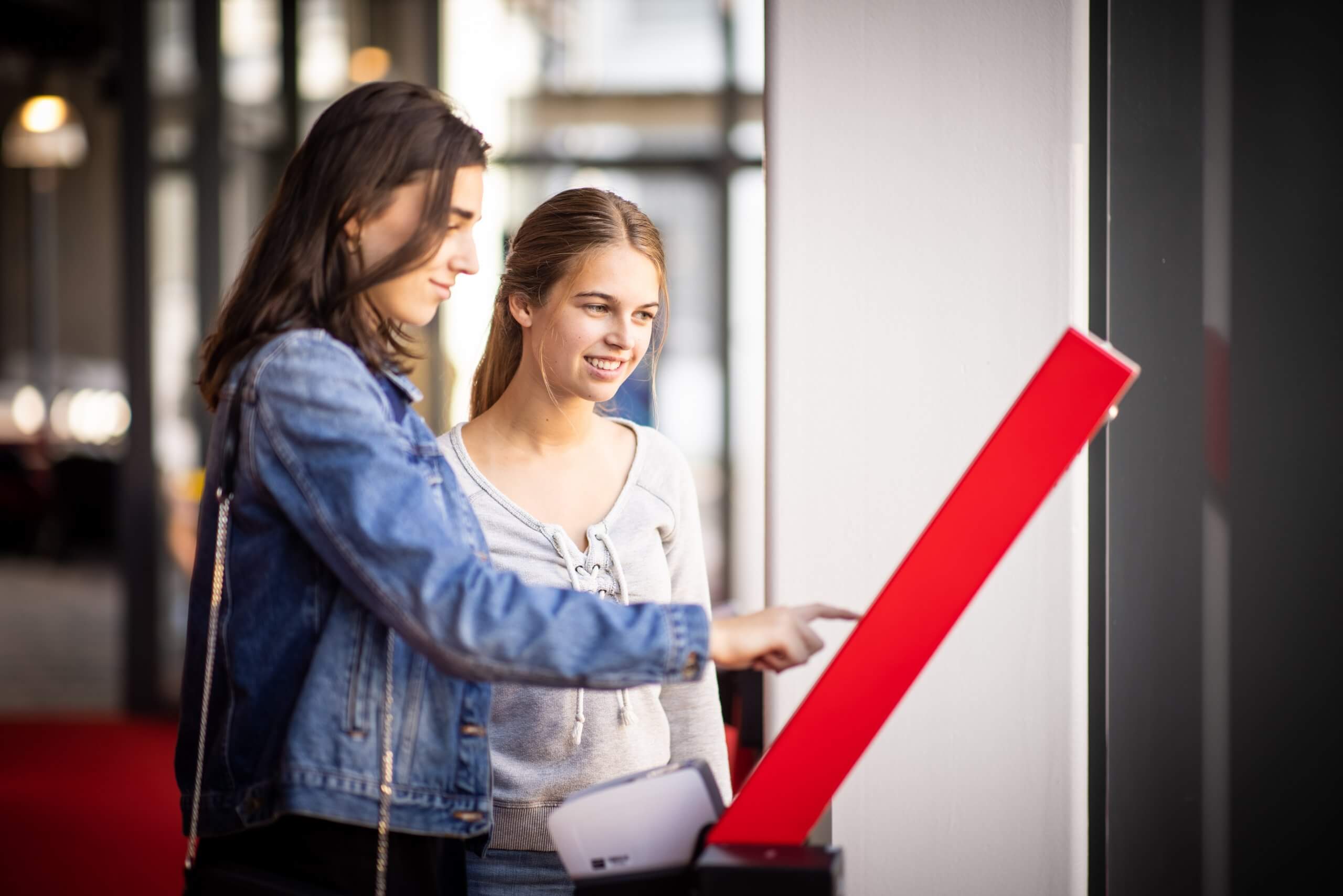 Twee vrouwen werken samen bij een touchscreen-kiosk in een lichte binnenruimte.