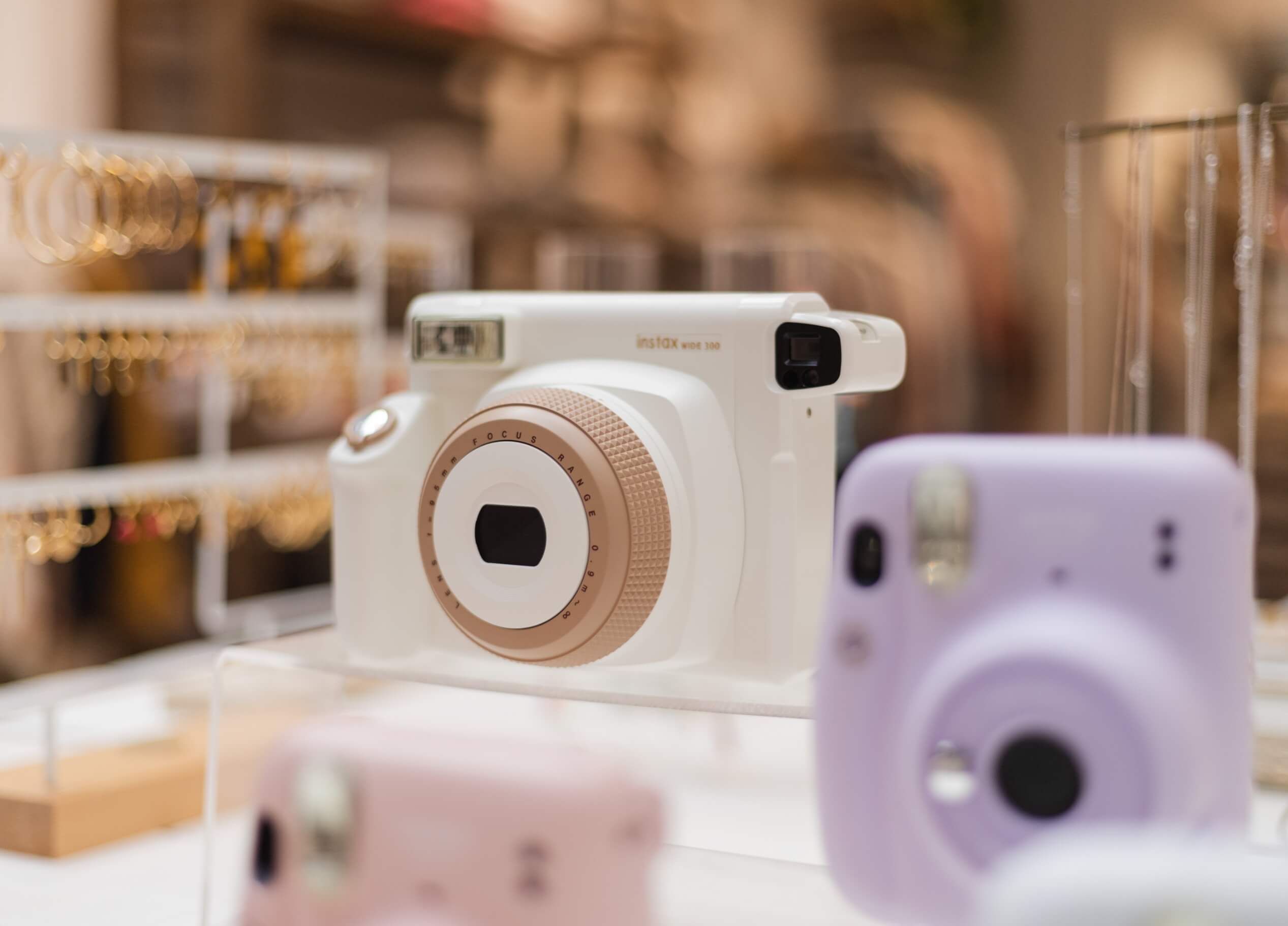 Een wit- en roségouden instantcamera schittert tussen de pastelkleurige camera's in een chique etalage.